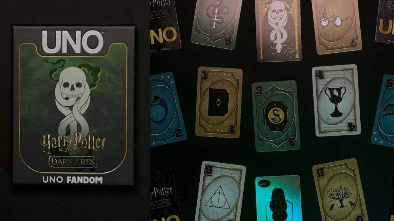 Caixa do jogo UNO Harry Potter Dark Arts ao lado de várias cartas temáticas espalhadas sobre uma superfície escura.