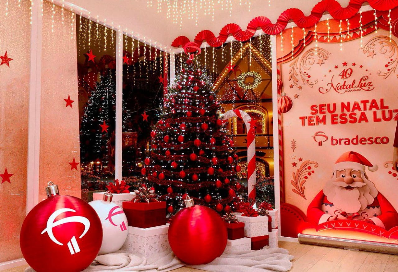 Decoração de Natal do Bradesco no Natal Luz de Gramado com uma árvore de Natal iluminada em vermelho, grandes bolas decorativas da marca e um banner do Papai Noel.